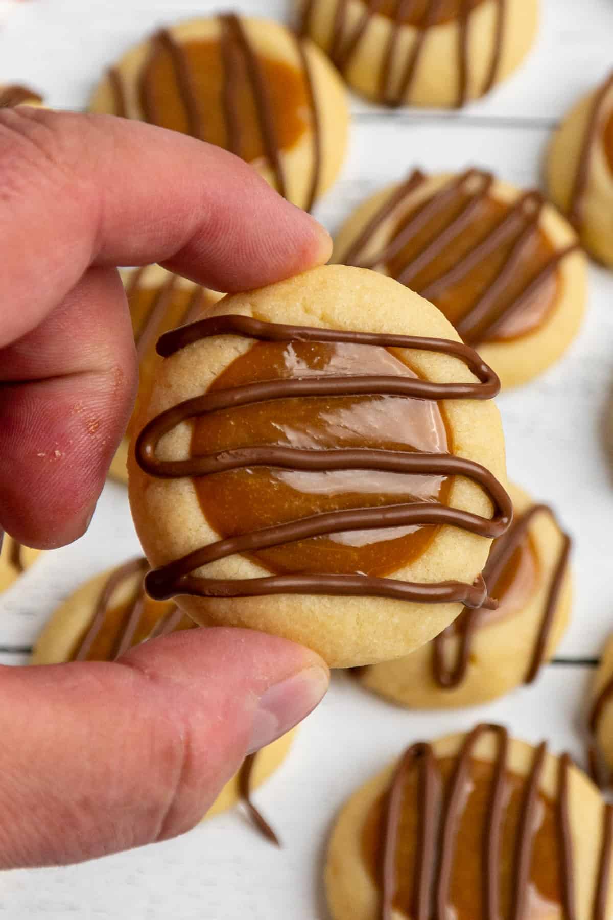 Close up of a hand holding a twix thumbprint cookie
