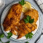 Two air fryer chicken breasts on a plate with one that has been sliced up