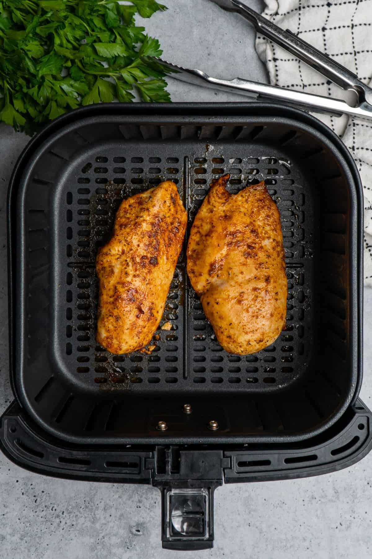 Two cooked chicken breasts in an air fryer basket