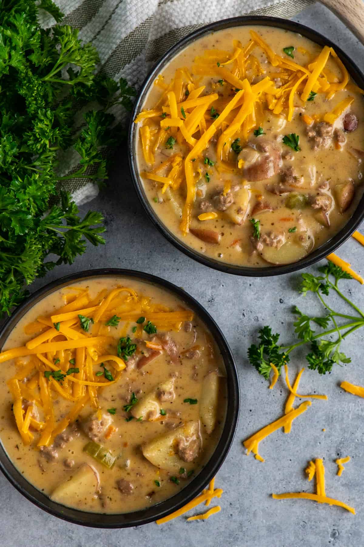Two bowls of the best cheeseburger soup garnished with cheese and parsley.