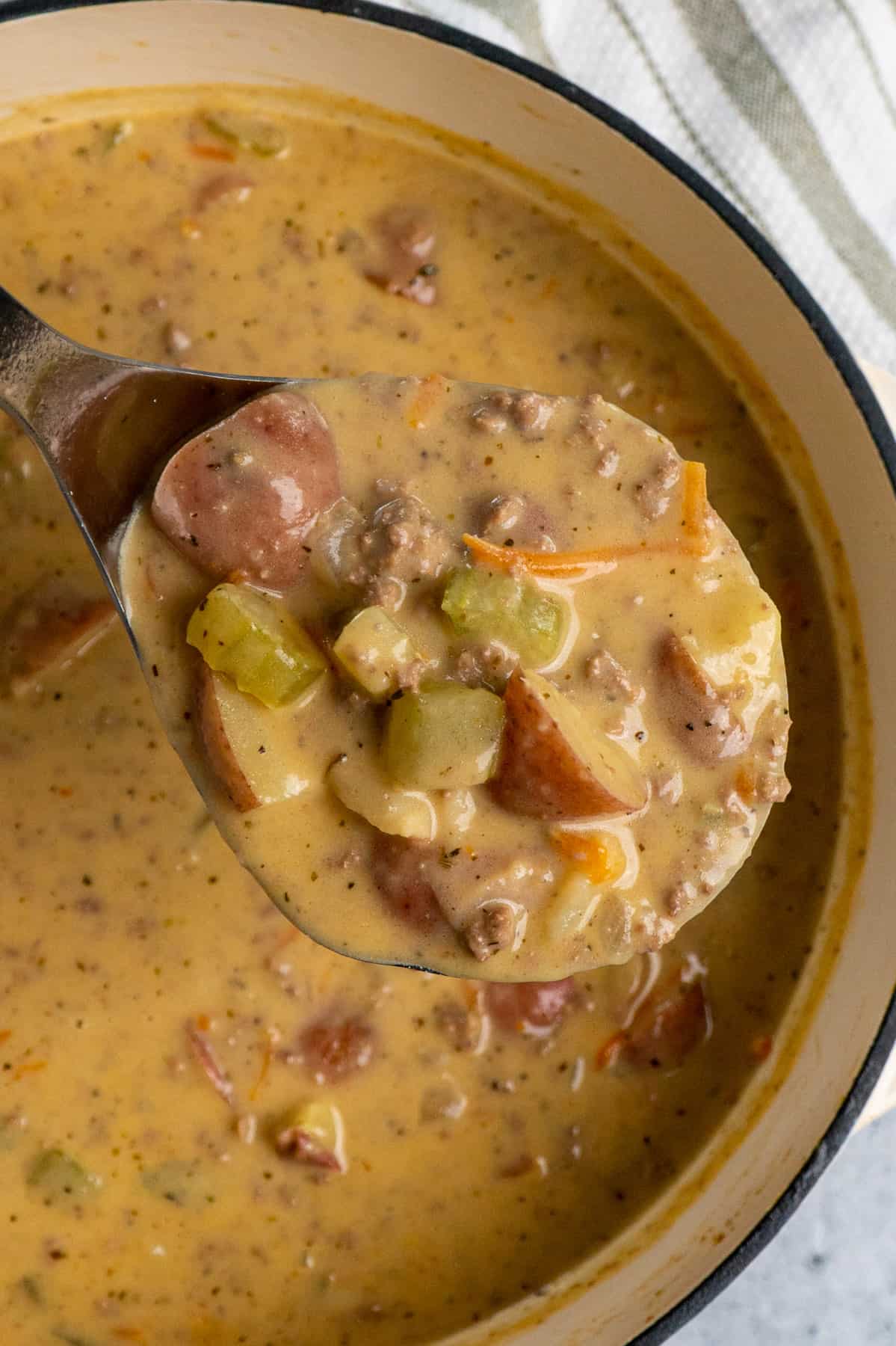 Cheeseburger soup in a laddle over a pot.