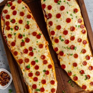 Baked French bread pizza on wood cutting board.