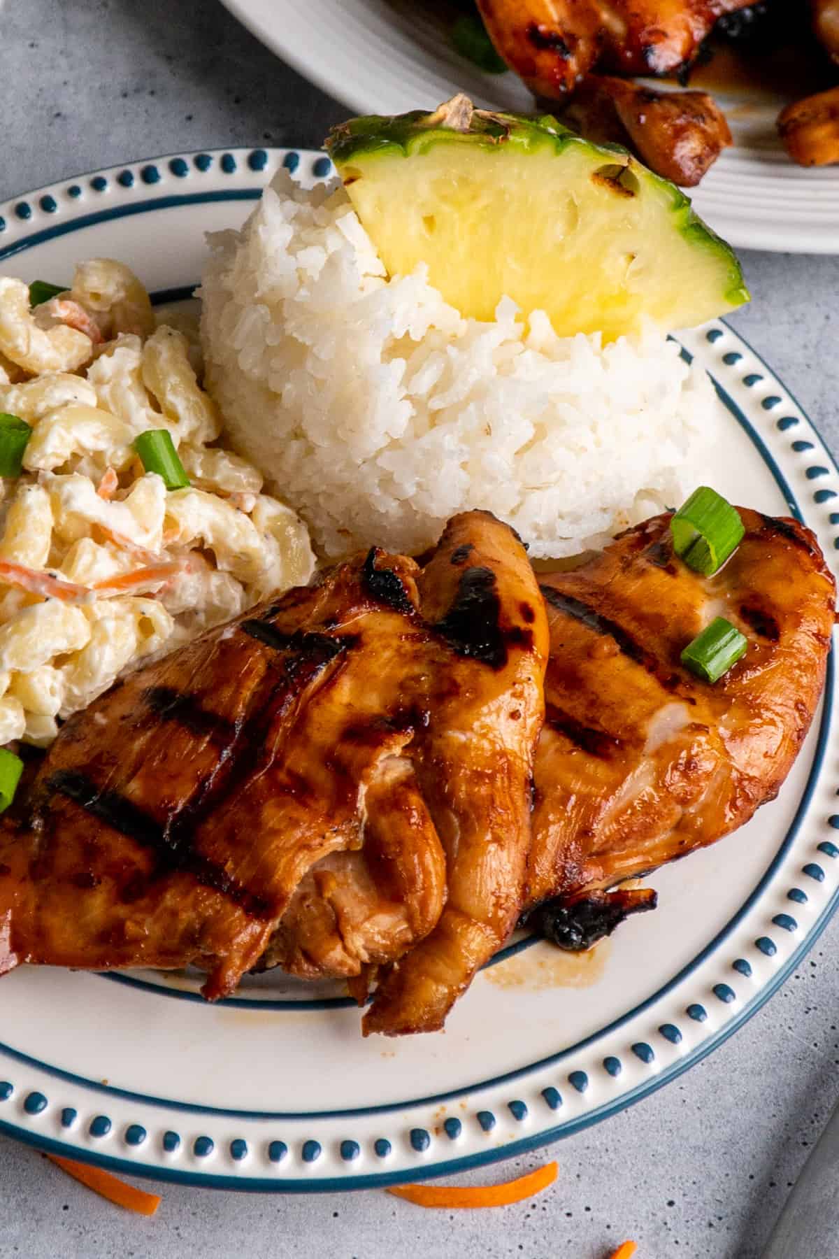 Marinated chicken thighs on a plate with macaroni salad and rice.