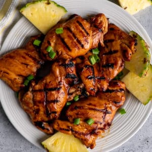 Grilled teriyaki chicken thighs on a plate with pineapple.