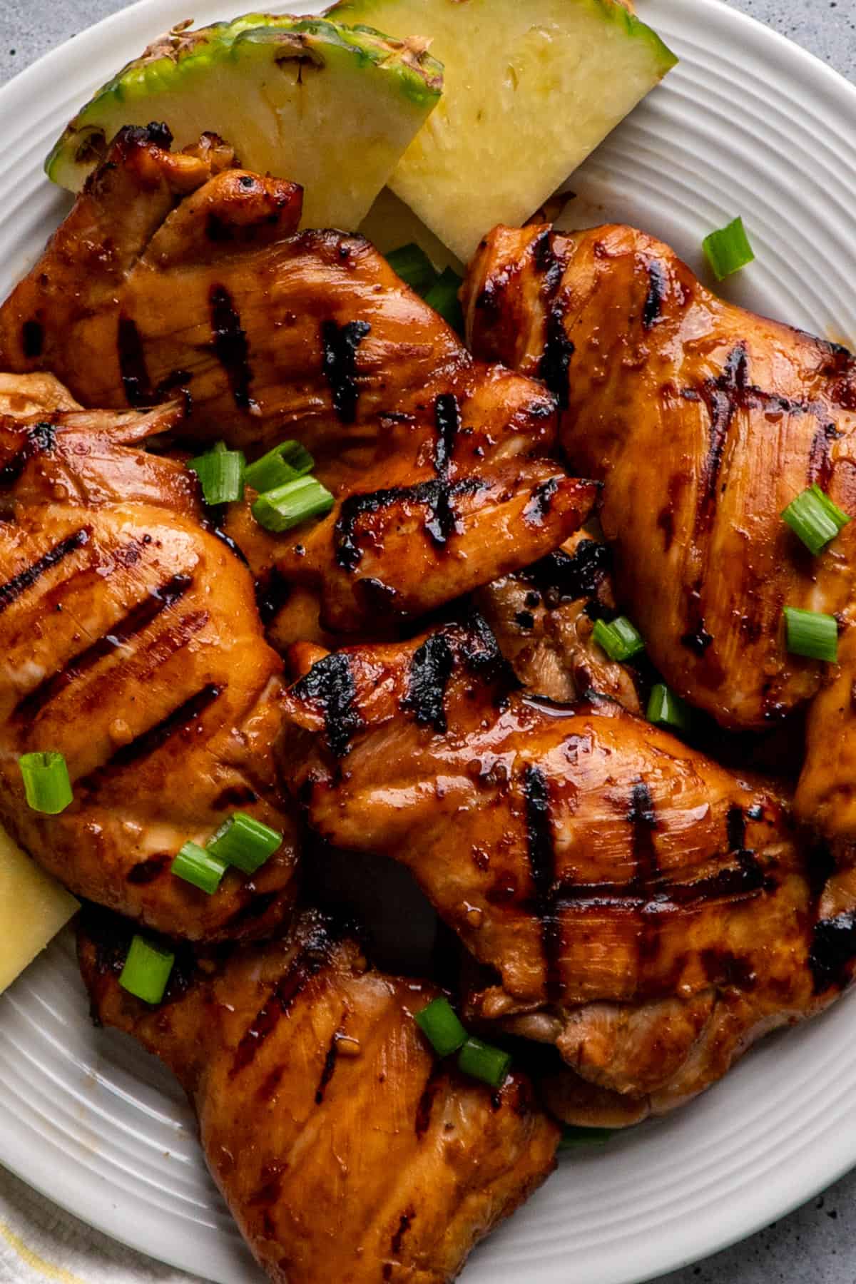 Close-up of grilled teriyaki chicken thighs on a plate with pineapple.