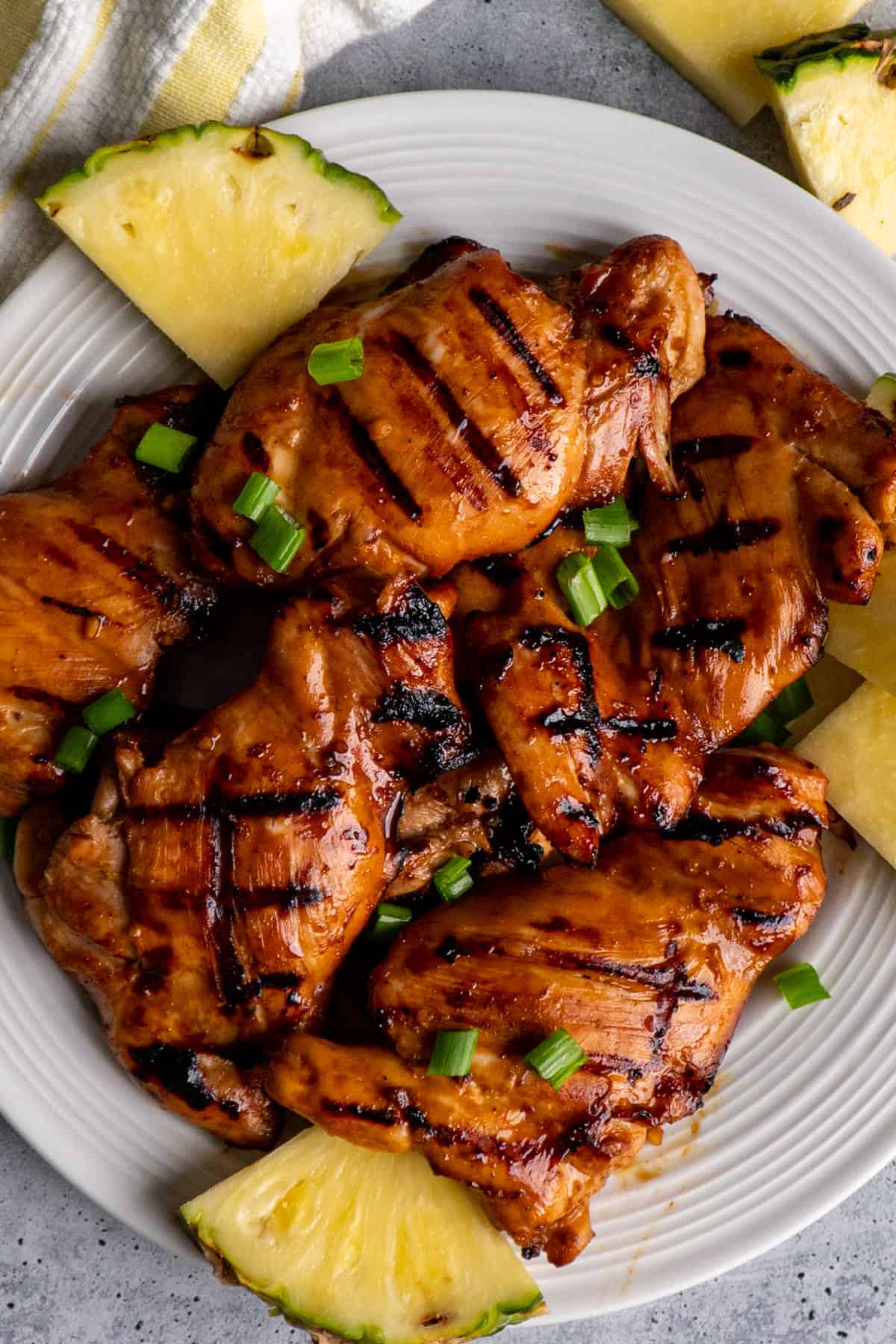 Grilled teriyaki chicken thighs on a plate with pineapple.