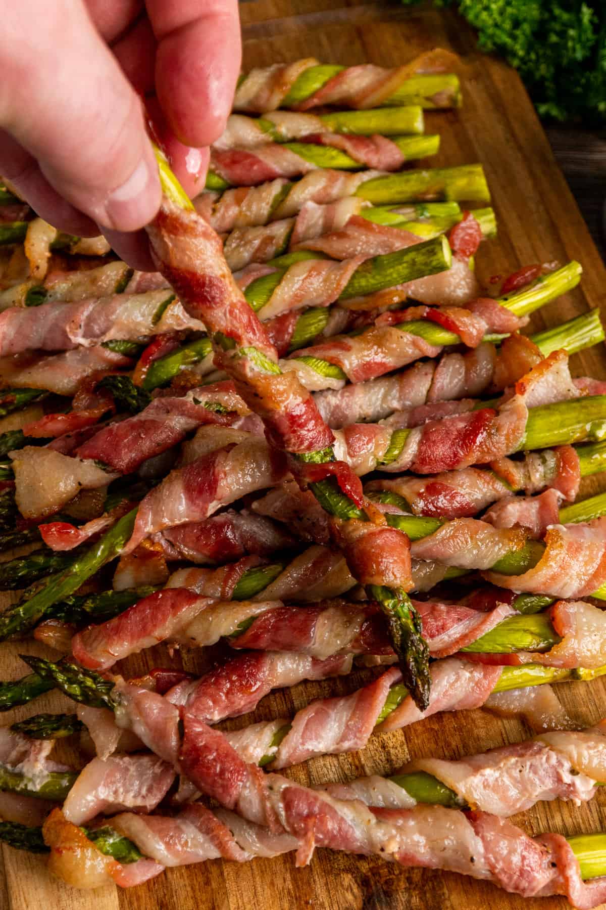 A hand holding a piece of bacon wrapped asparagus.