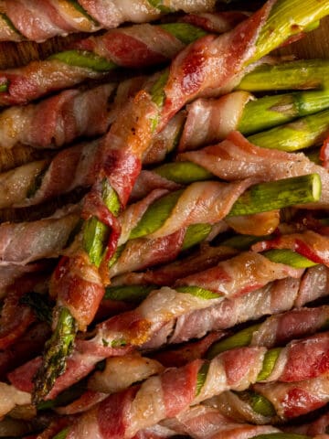 Close up of bacon wrapped asparagus on a wood cutting board.