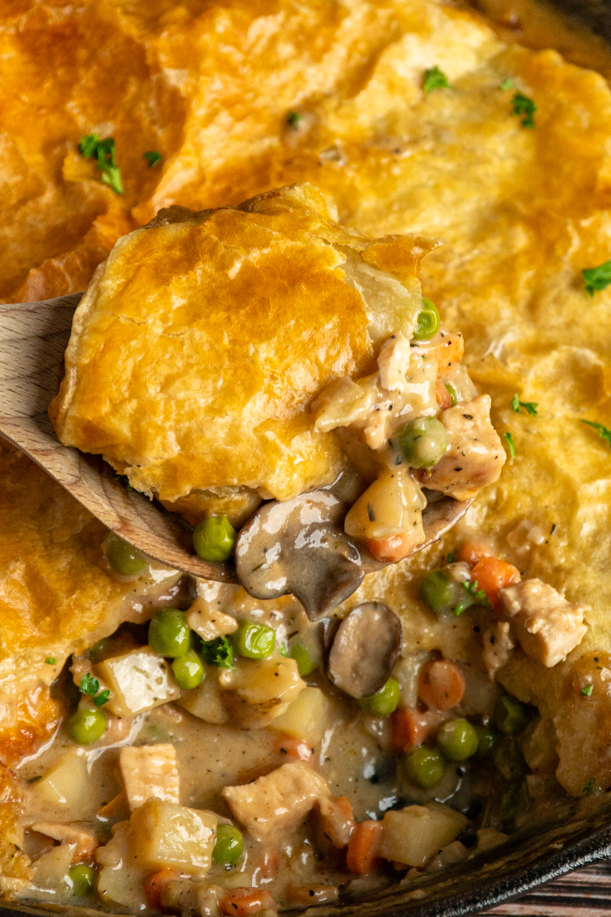 Close-up of puff pastry chicken pot pie on a wooden spoon.
