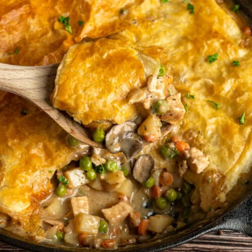 Close-up of puff pastry chicken pot pie on a wooden spoon.