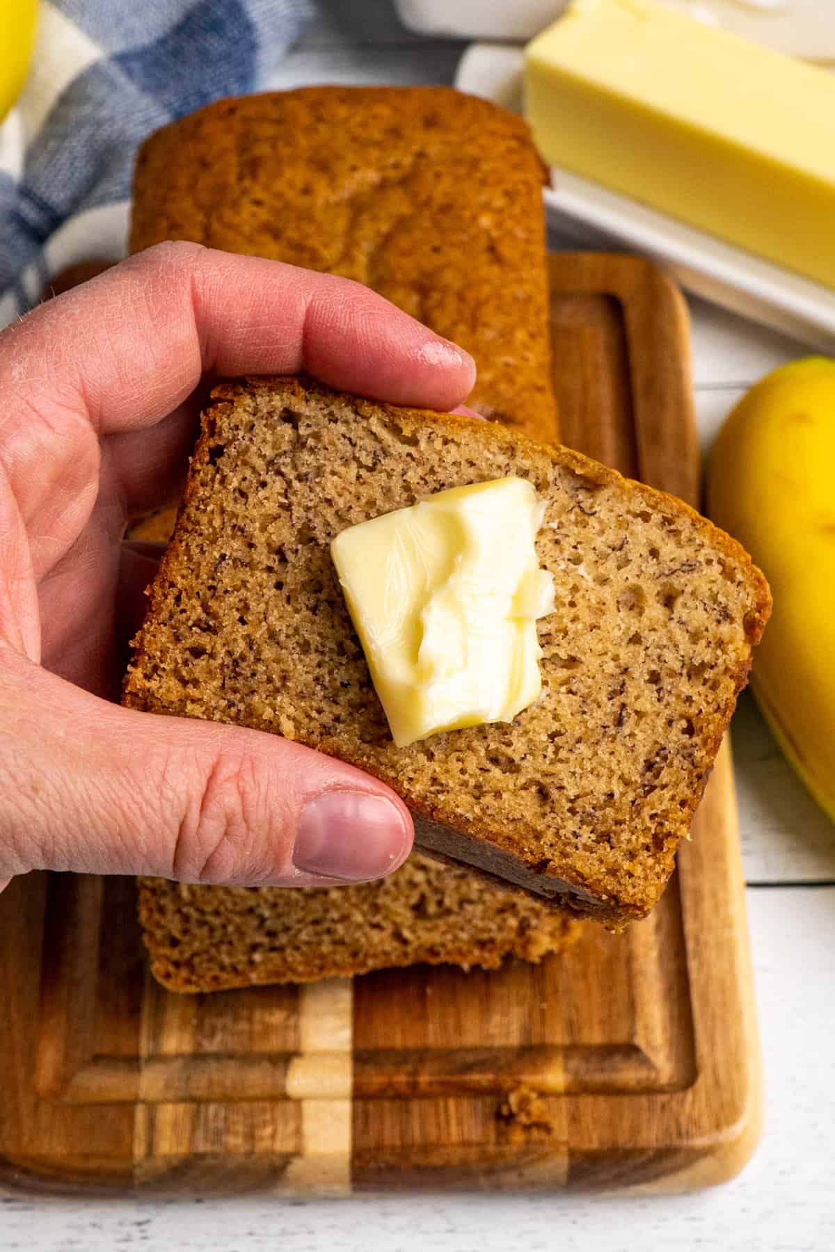 A hand holding a piece of banana bread with butter on it.