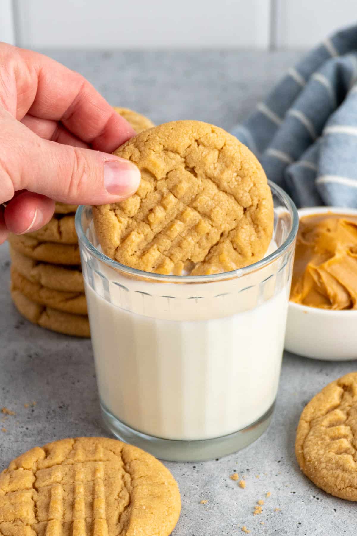 A hand dipping a peanut butter cookie in a glass of milk.