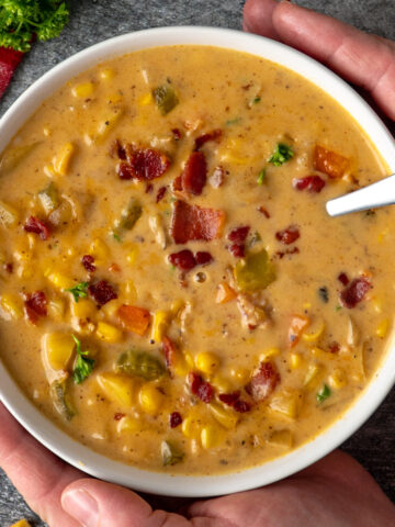 Hands holding a bowl of creamy corn chowder.