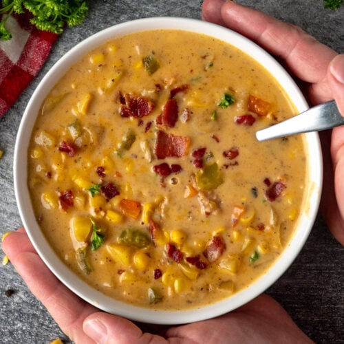Hands holding a bowl of creamy corn chowder on the table.