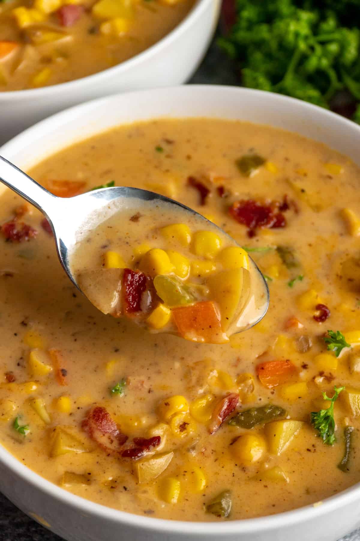 A spoonful of corn chowder over a bowl.
