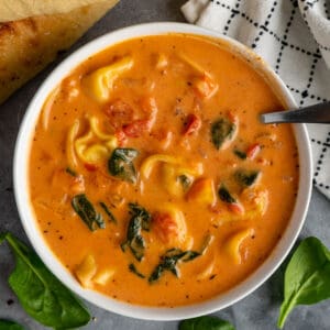 Creamy tortellini soup in a white bowl with spinach.