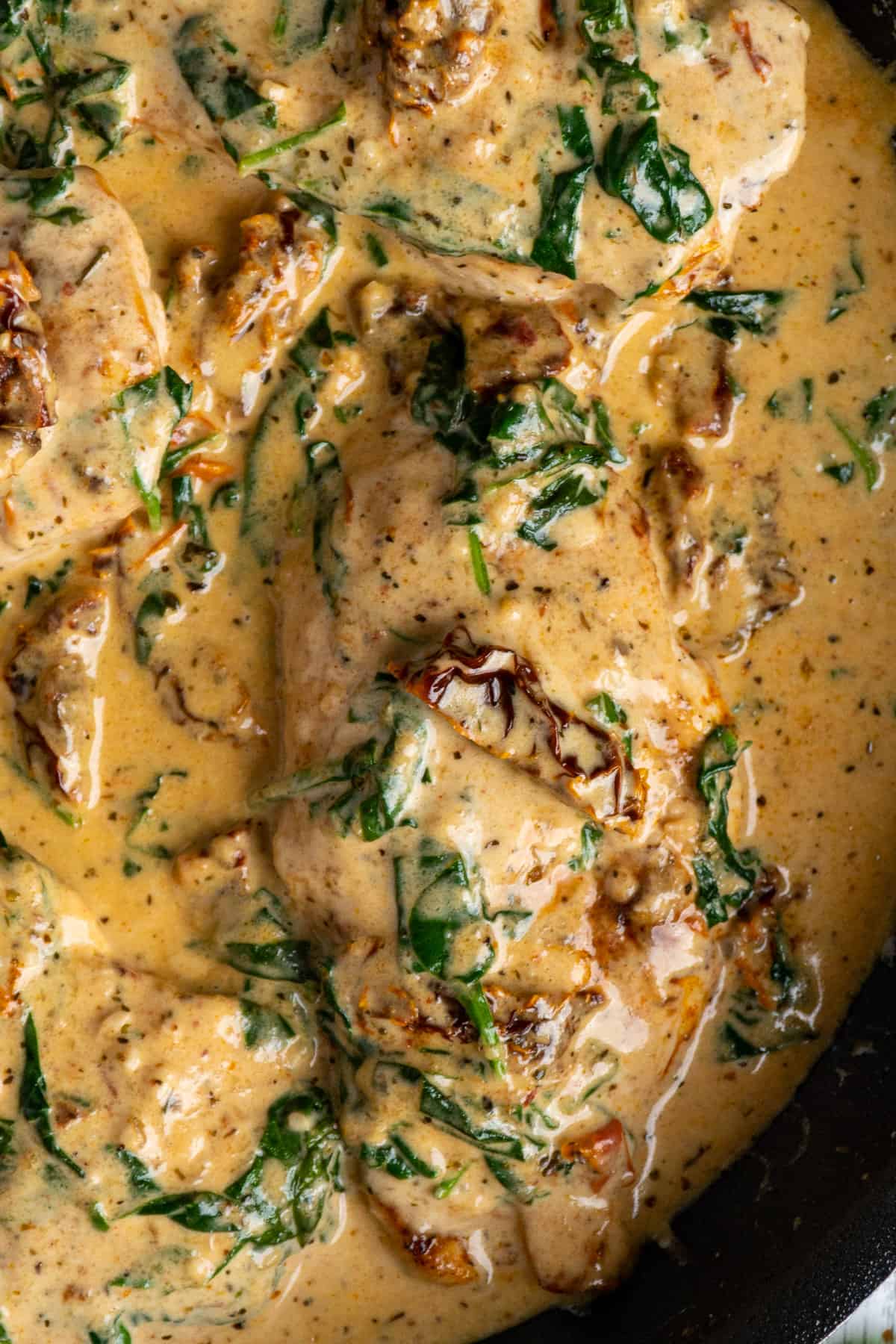 Close up of chicken with a creamy sauce, spinach and sun dried tomatoes.