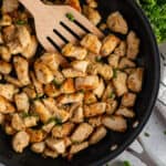 Garlic butter chicken bites in a skillet with a wooden spatula.