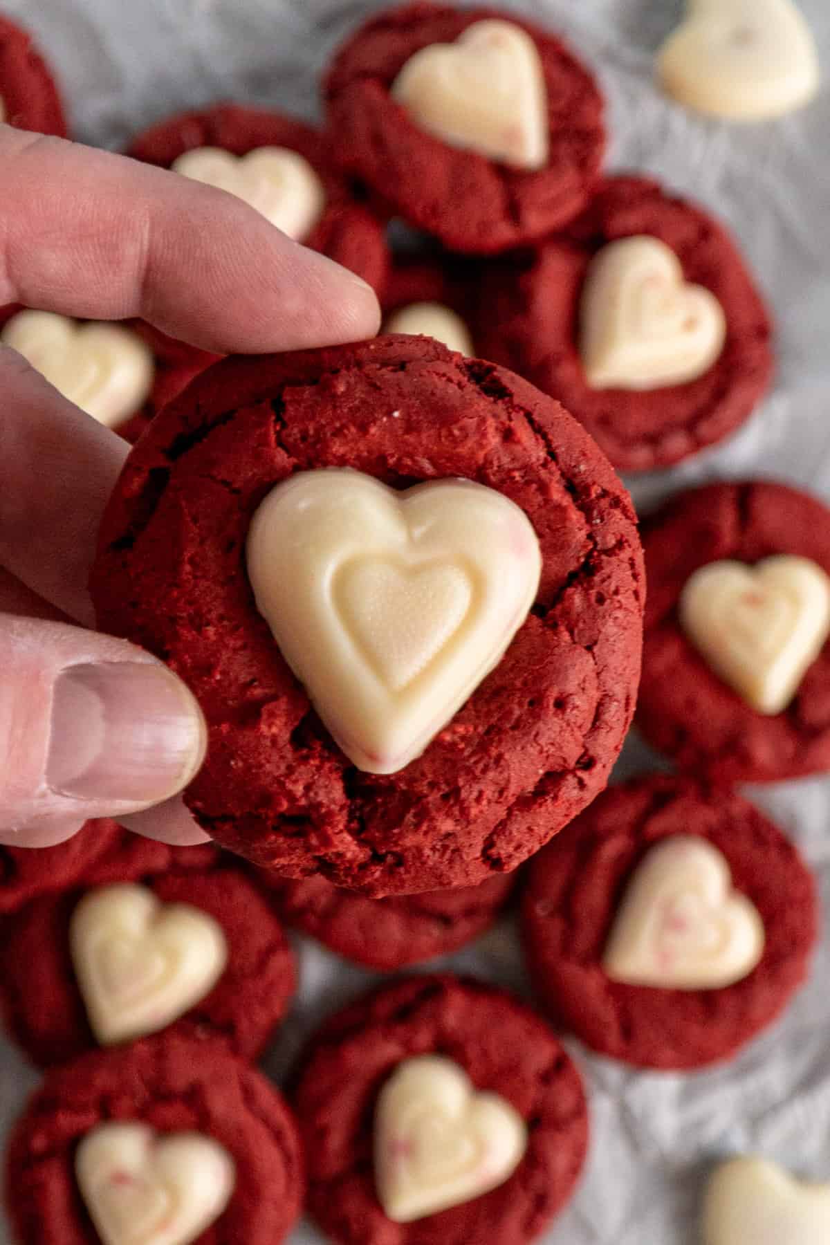 A hand holding a cookie with a chocolate heart in the center of it.
