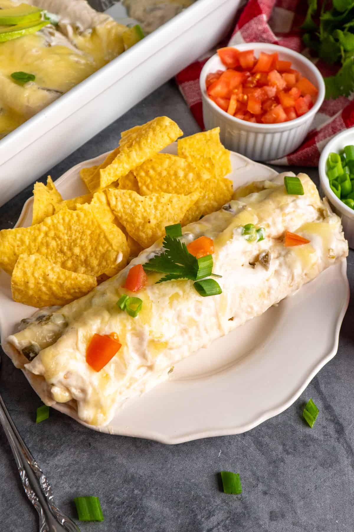 Sour cream enchilada on a white plate with tortilla chips.