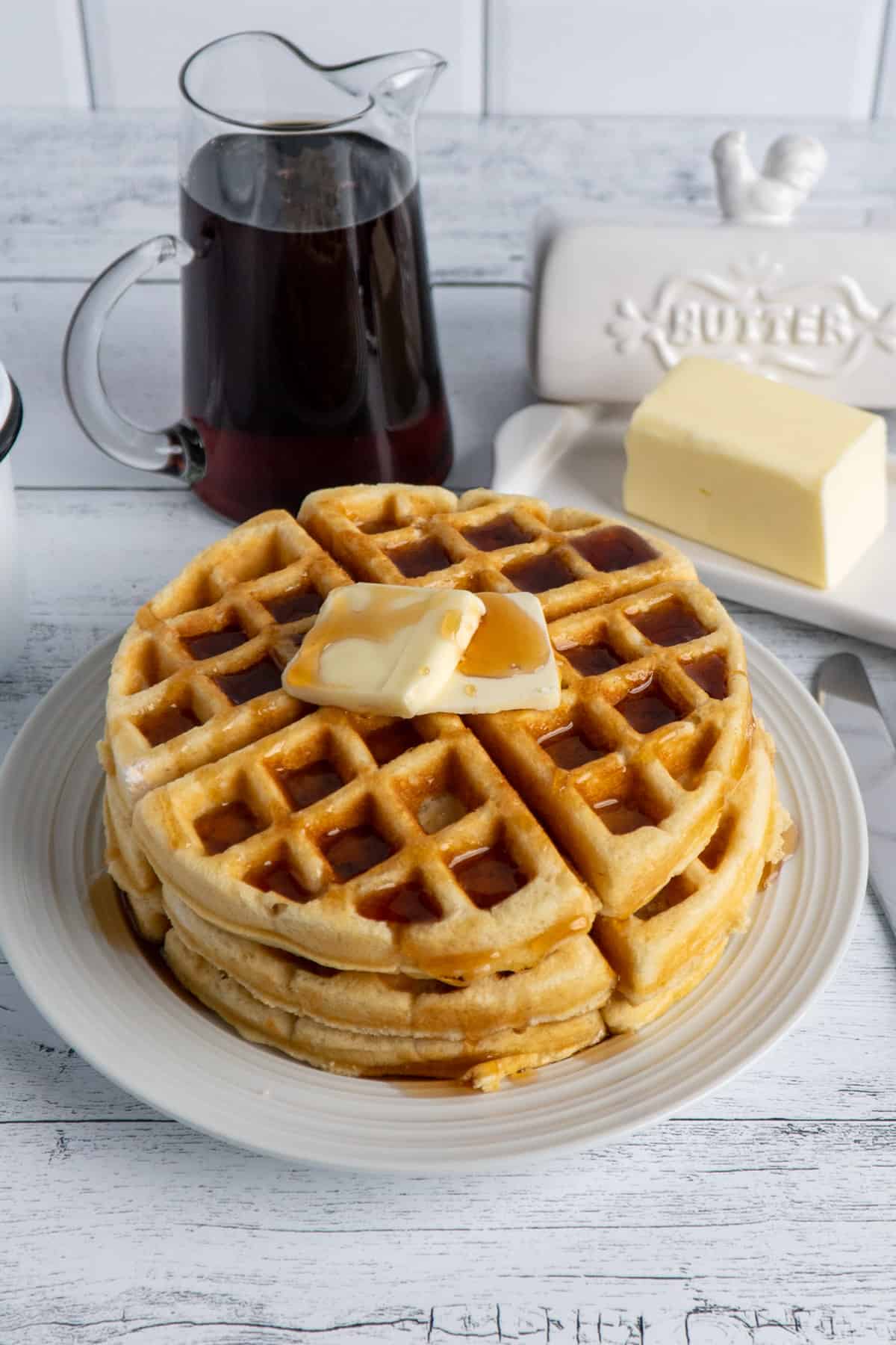 Homemade waffles stacked on top of each other with syrup and butter.