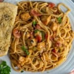 Close-up of chicken spaghetti on a plate with a slice of garlic bread.