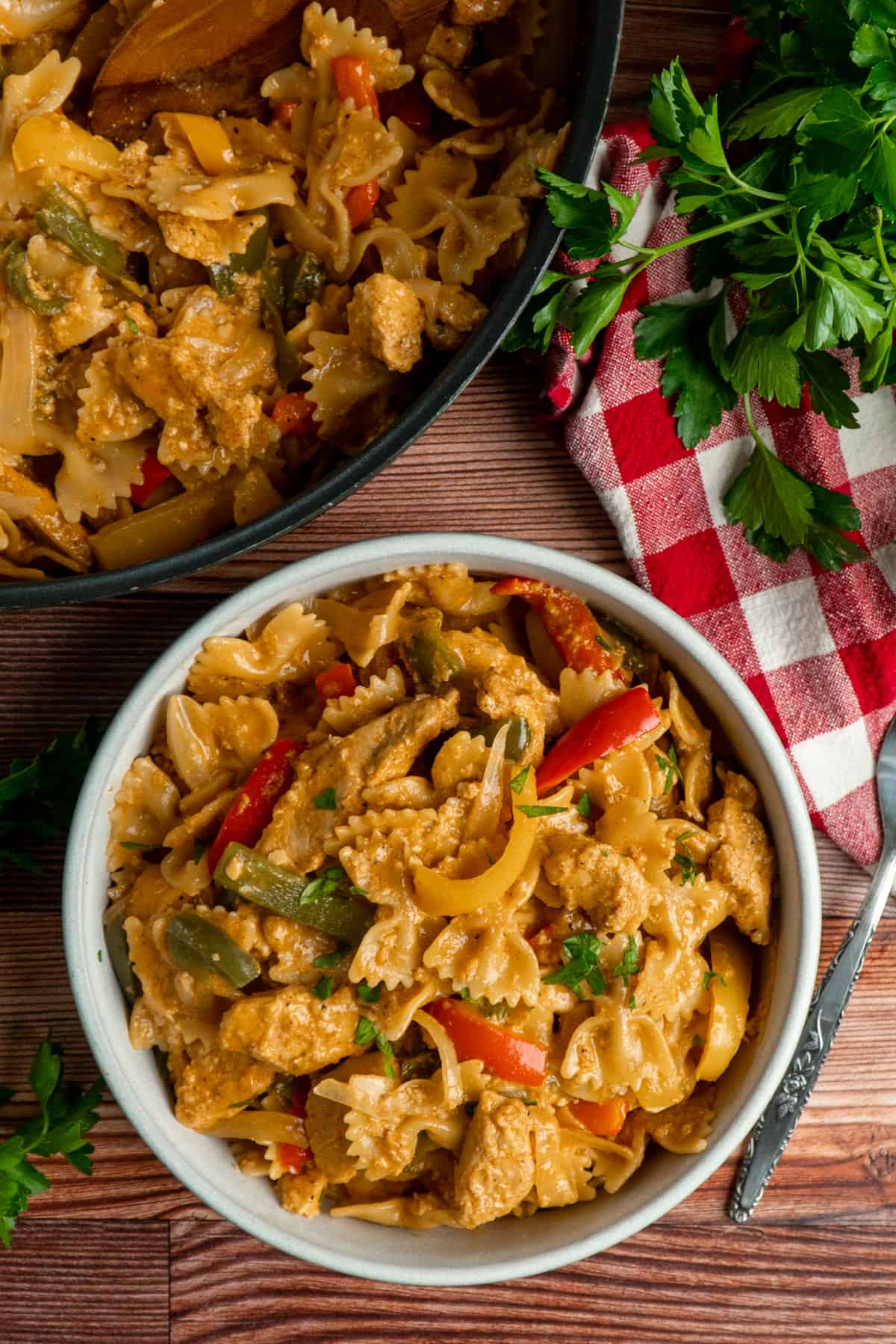 A bowl of chicken fajita pasta with a skillet in the background.