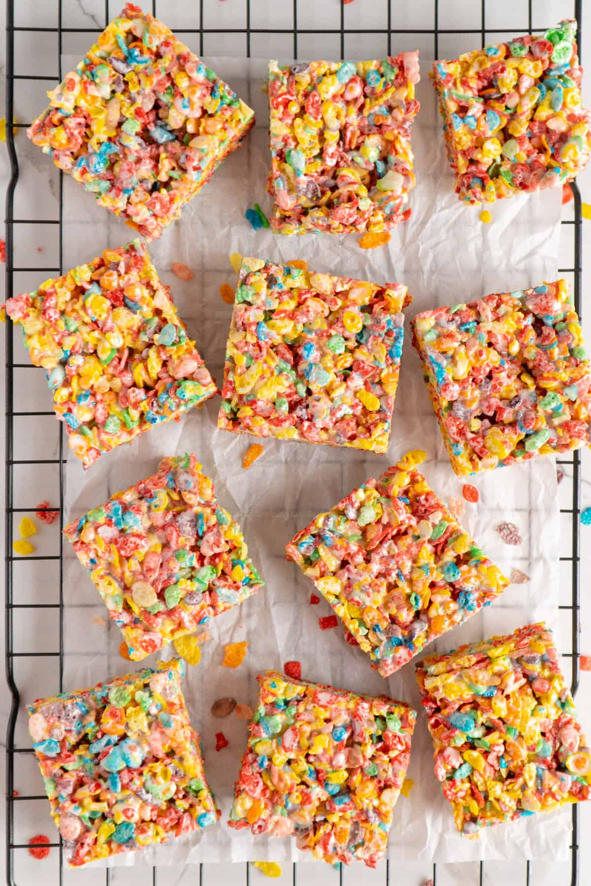 Fruity pebbles rice crispy treats on a piece of parchment paper on a cooling rack.