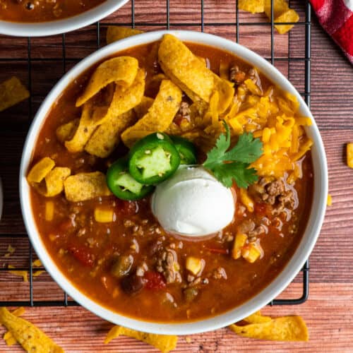 Taco soup in a white bowl and garnished with Fritos, cheese, and sour cream.