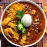 Taco soup in a white bowl and garnished with Fritos, cheese, and sour cream.