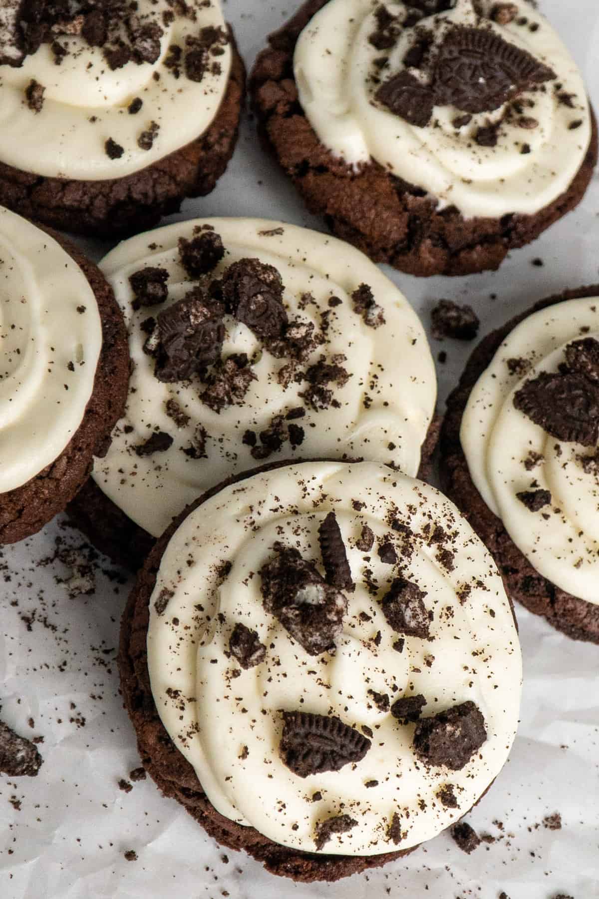 Overhead image of chocolate Oreo cookies with frosting stacked on each other on parchment paper.