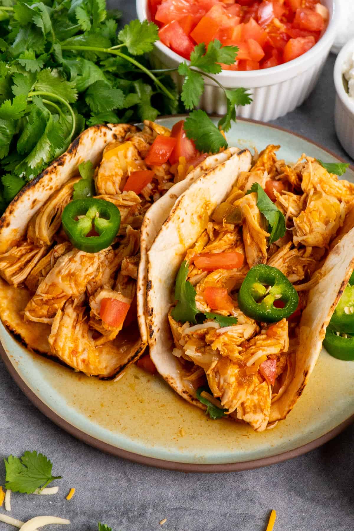 Two chicken tacos garnished with cheese, tomatoes, and jalapenos.