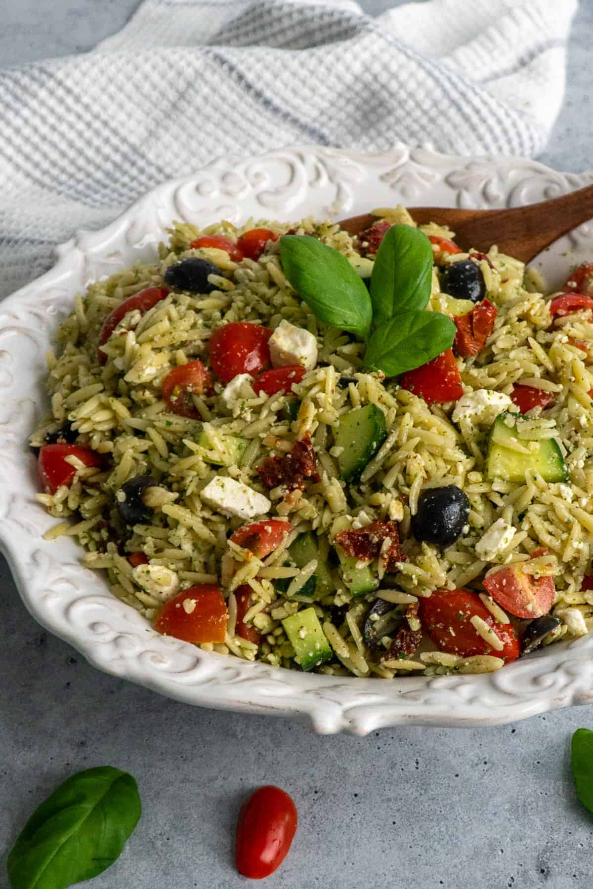 Close up of Pesto orzo pasta salad with tomatoe and feta cheese in a white bowl.