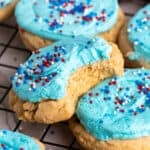 A frosted sugar cookie with a bite taken out of it.