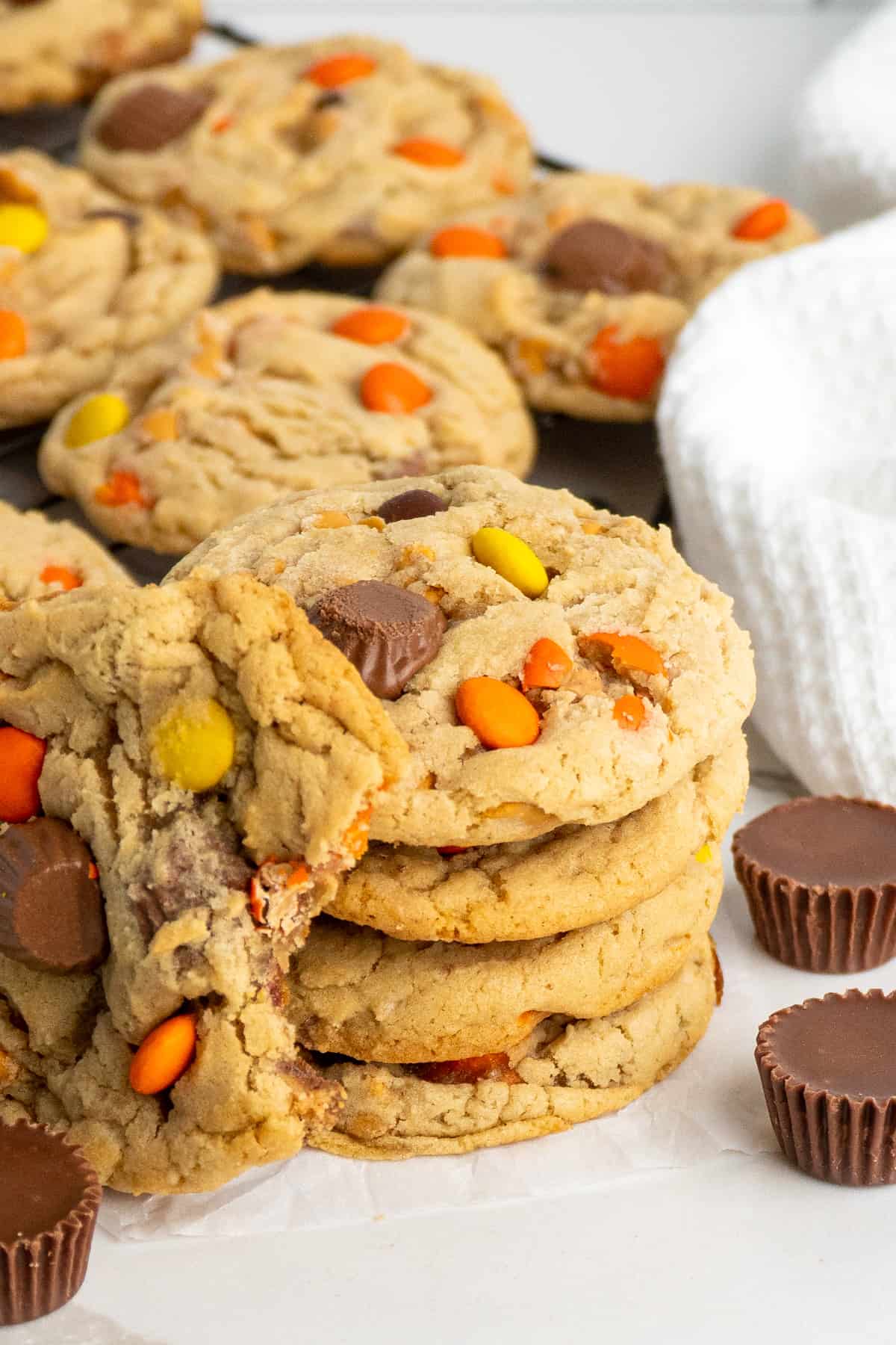 Four Reese's pieces cookies stacked on each other with one on the side with a bite taken out of it.