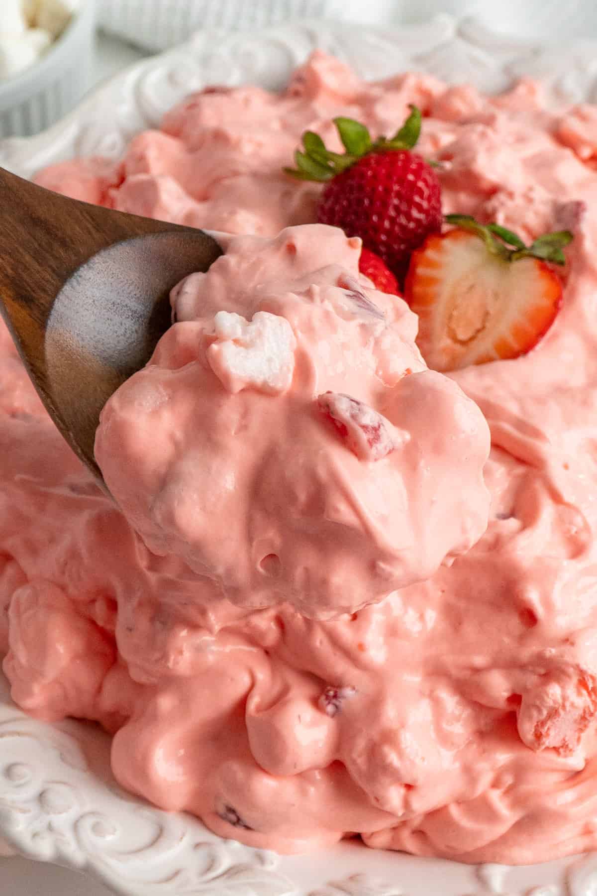 A wooden spoon holding a scoop of strawberry fluff salad.