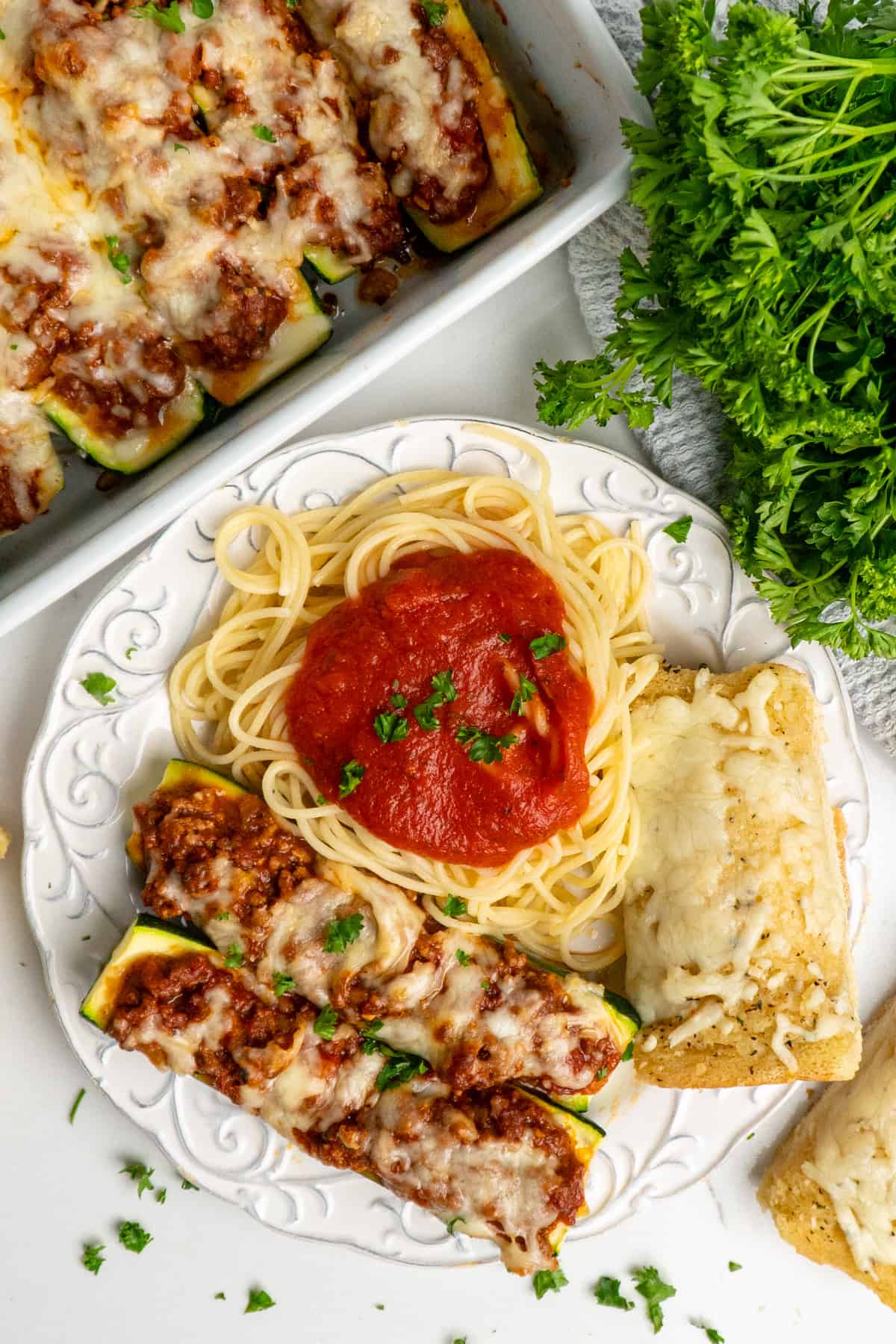 Two stuffed zucchini boats on a plate with pasta and bread.