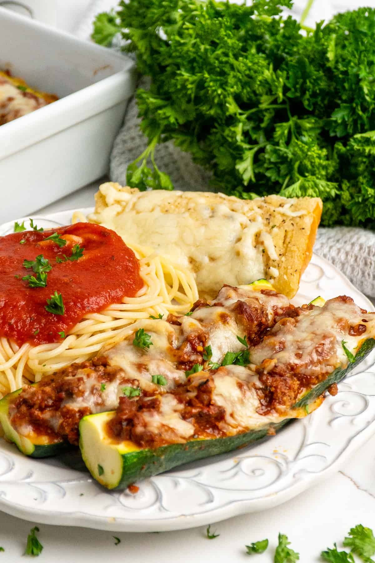 Close-up of two stuffed zucchini boats on a plate with pasta and bread.