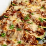 Stuffed zucchini boats with ground beef in a white baking dish.