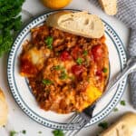Baked ravioli on a plate with a piece of bread.