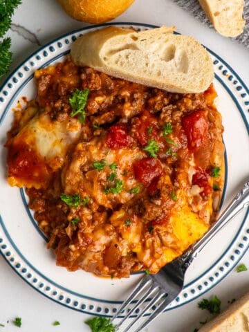Overhead, look at baked ravioli on a plate with a piece of bread.