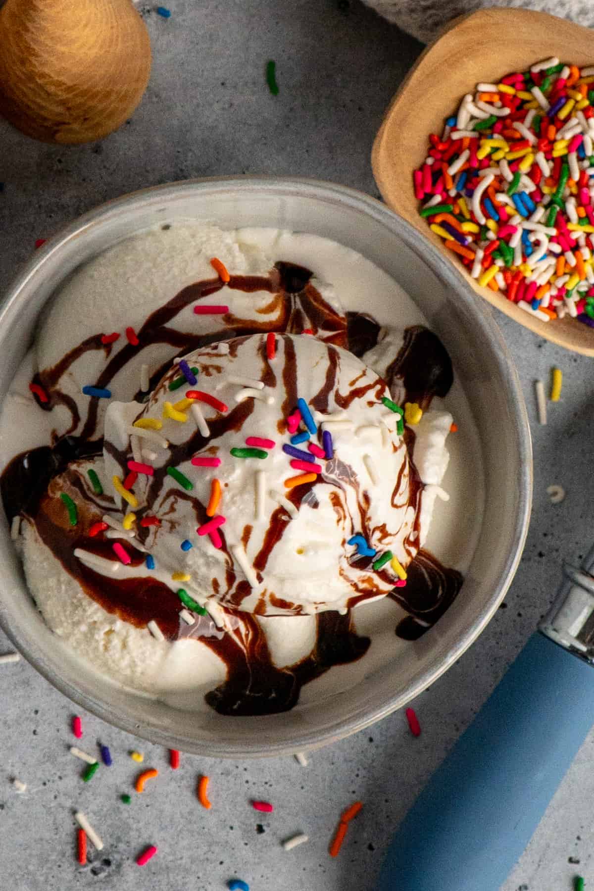 Overhead look at vanilla ice cream with chocolate sauce and sprinkles on top.
