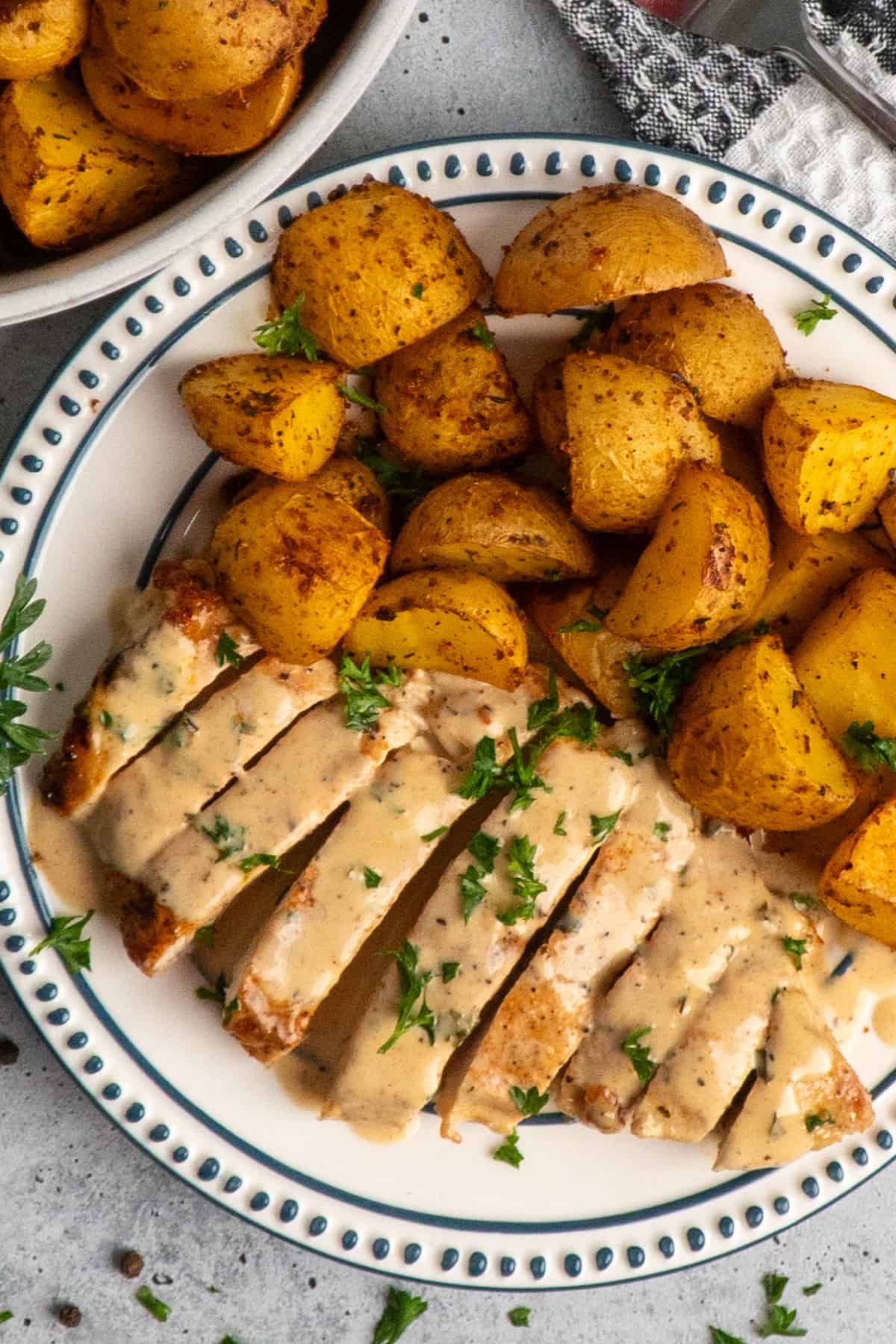 Creamy ranch chicken on a plate with roasted potatoes.