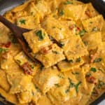 Overhead, look at cream Tuscan ravioli in a skillet with a wooden spoon.
