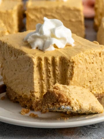 Close-up of a no-bake pumpkin cheesecake bars on a plate with whipped cream on top.