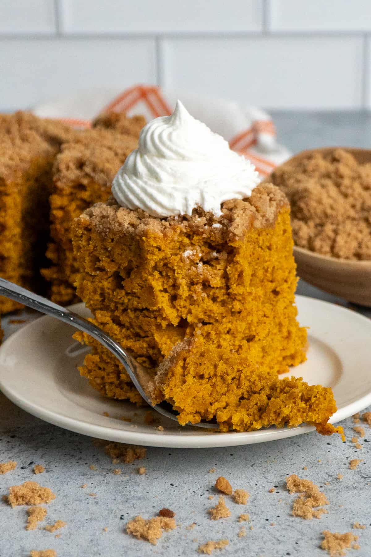 A piece of pumpkin coffee cake on a plate with whipped cream on top.