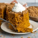 A piece of pumpkin coffee cake on a plate with whipped cream on top.