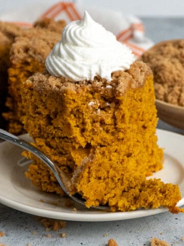 A piece of pumpkin coffee cake on a plate with whipped cream on top.