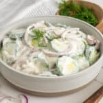 Creamy cucumber salad in a bowl with dill in the background.