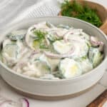 Side view of creamy cucumber salad in a bowl with dill in the background.